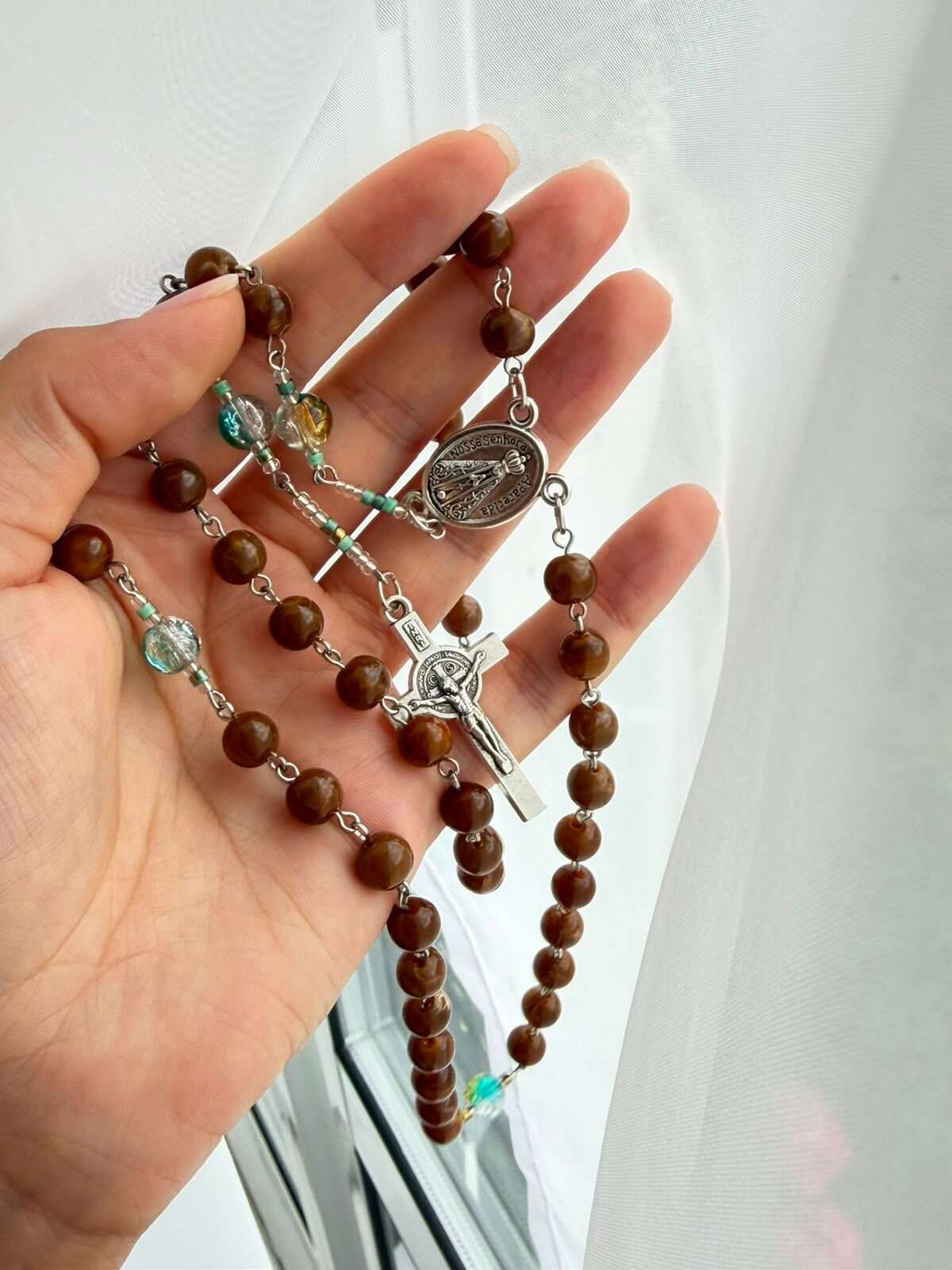 Brown marbled beads on fine wire links, laid open across a palm, with an oval centre medal and a small crucifix catching the window light