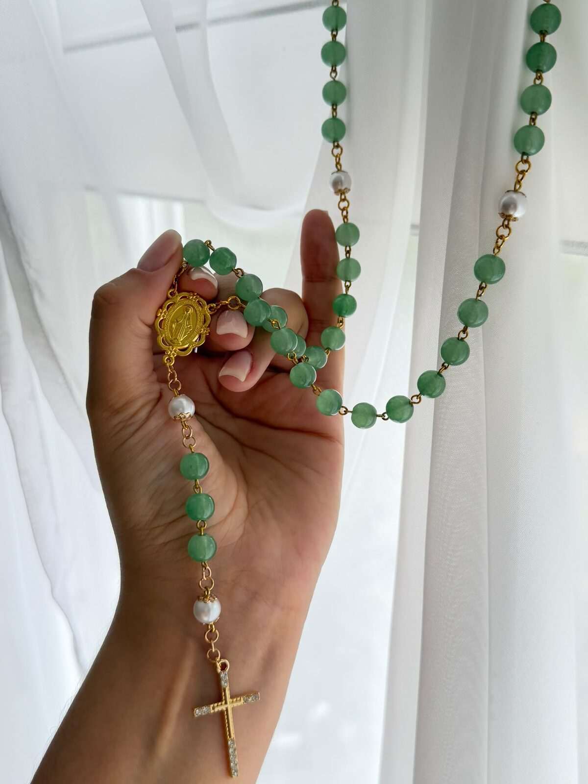 Bright green beads on warm-toned wire links falling from a raised hand, white round notes at the decades, an oval centre and a slender cross set with clear points