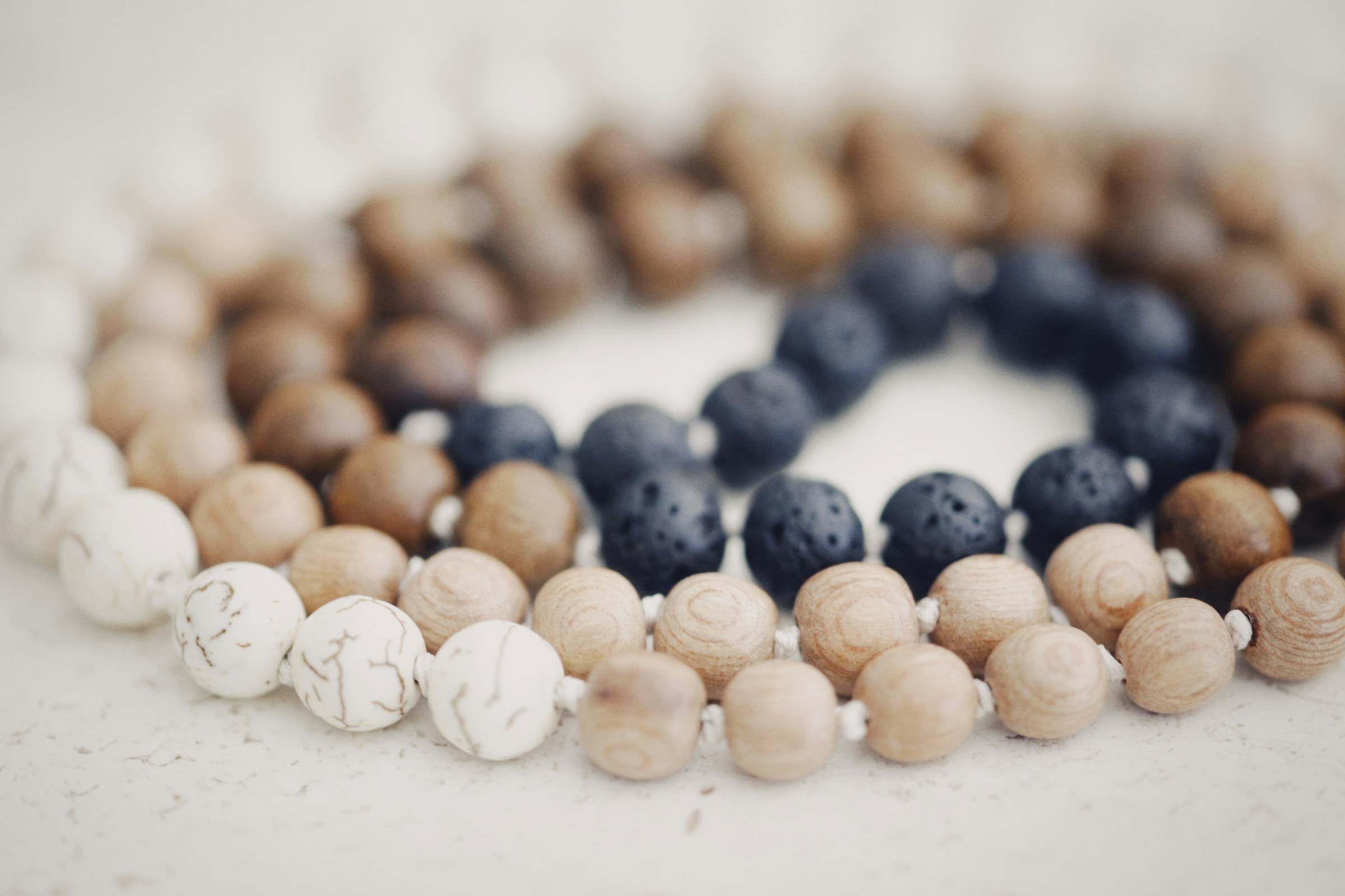 A full strand of pale wooden and dark stone beads, laid in a slow curve across white linen