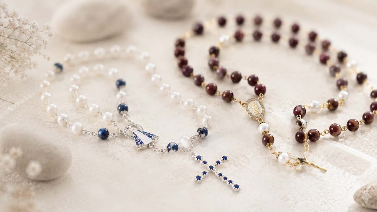 Two full strands laid side by side on a pale surface, each bead turned onto its own link, a cross at the end of each